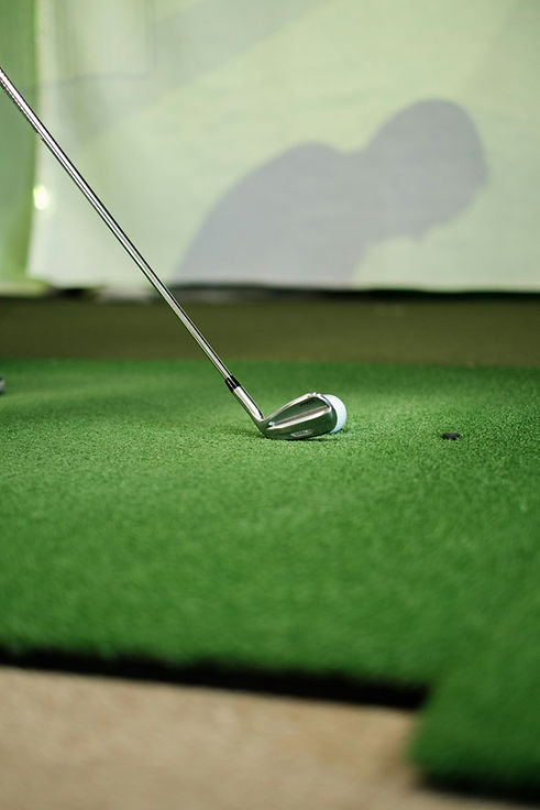 Golf club lined up with ball in front of golf sim