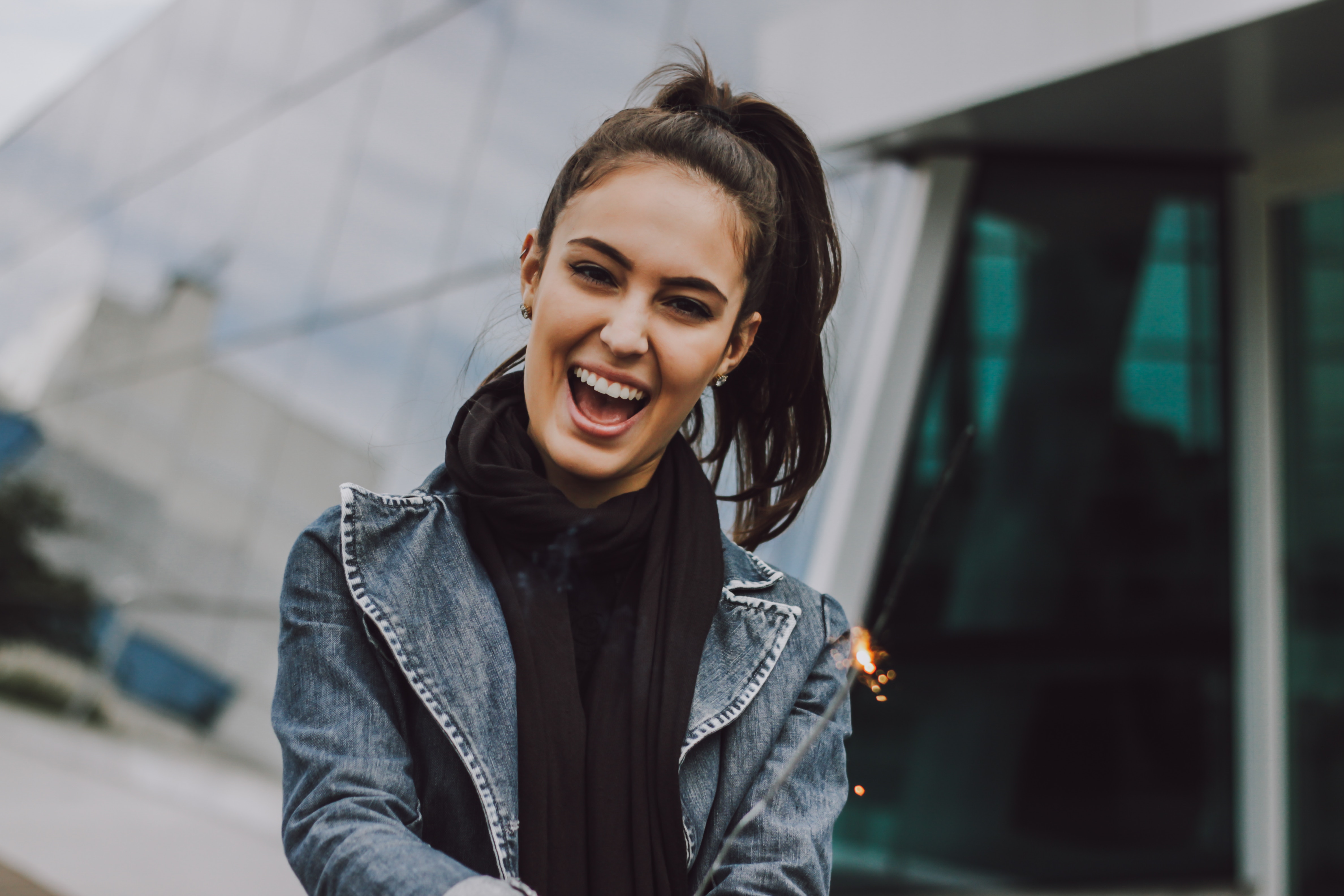 Smiling woman wearing a denim jacket and scarf, sparkling light in background.