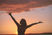 Silhouette of a woman with arms outstretched against a vibrant orange sunset. Weight loss counseling that addresses emotional eating and inner peace.