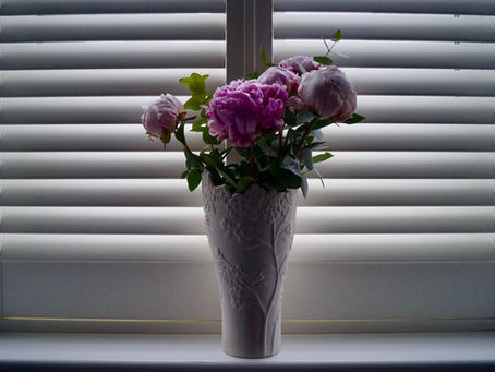 A bouquet of flowers in a decorative vase in front of white interior shutters.