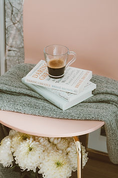 white flowers, pink chair with gold legs, grey blanket, three white books, coffee in clear mug
