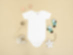 A white baby onesie, baby socks, a pacifier, a teddy bear and two teethers