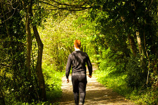 Teen walking along a quiet forest path surrounded by greenery, moving through soft natural light in a calm and reflective setting