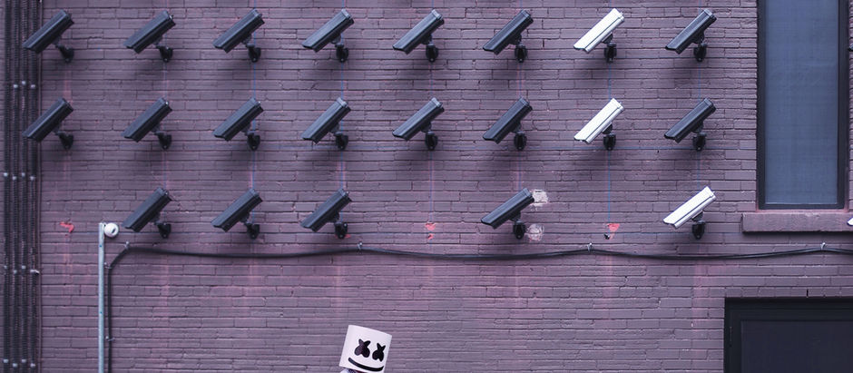 Surveillance cameras mounted on a brick wall with a person in a white outfit walking.