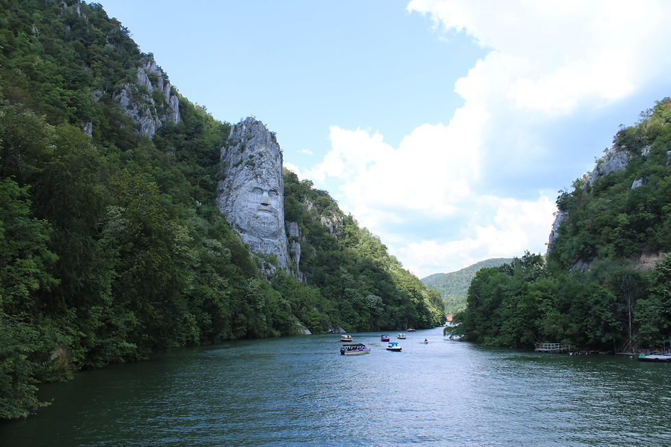 River flanked by lush hills, with a cliff face carved into a man's portrait. Boats dot the water under a partly cloudy blue sky.