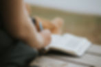 Woman sitting on a wooden deck, writing in her Bible