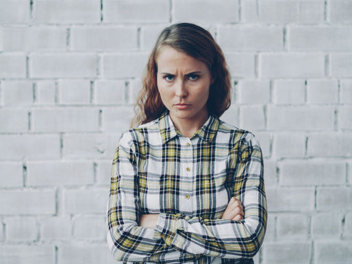 אישה עומדת עם ידיים שלובות ומבט סגור, מבטאת אכזבה וכעס פנימי בקשר קרוב