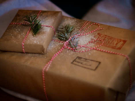 Brown paper-wrapped gifts with red string and green sprigs, dusted with snow. "Merry" stamped on one. Cozy, festive mood.