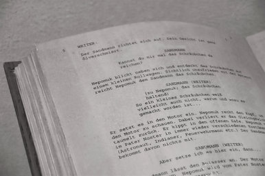 Close-up of a printed screenplay page in German, featuring character dialogue and stage directions, with visible page number formatting.