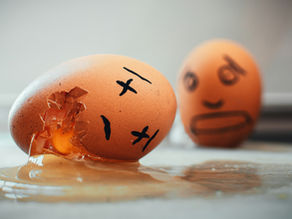 Cracked egg with a sad face spills yolk on a counter, while a blurred egg with a worried face sits behind it.