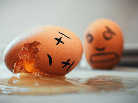 Cracked egg with a sad face spills yolk on a counter, while a blurred egg with a worried face sits behind it.