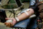 A person in uniform donating blood, arm with needle and bandages. Holding a gray ball. Medical equipment in the background.