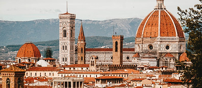 A panoramic view of Florence, Italy, featuring the red-tiled roofs, the Florence Cathedral with its iconic dome, and the tall bell tower, with rolling hills in the background.