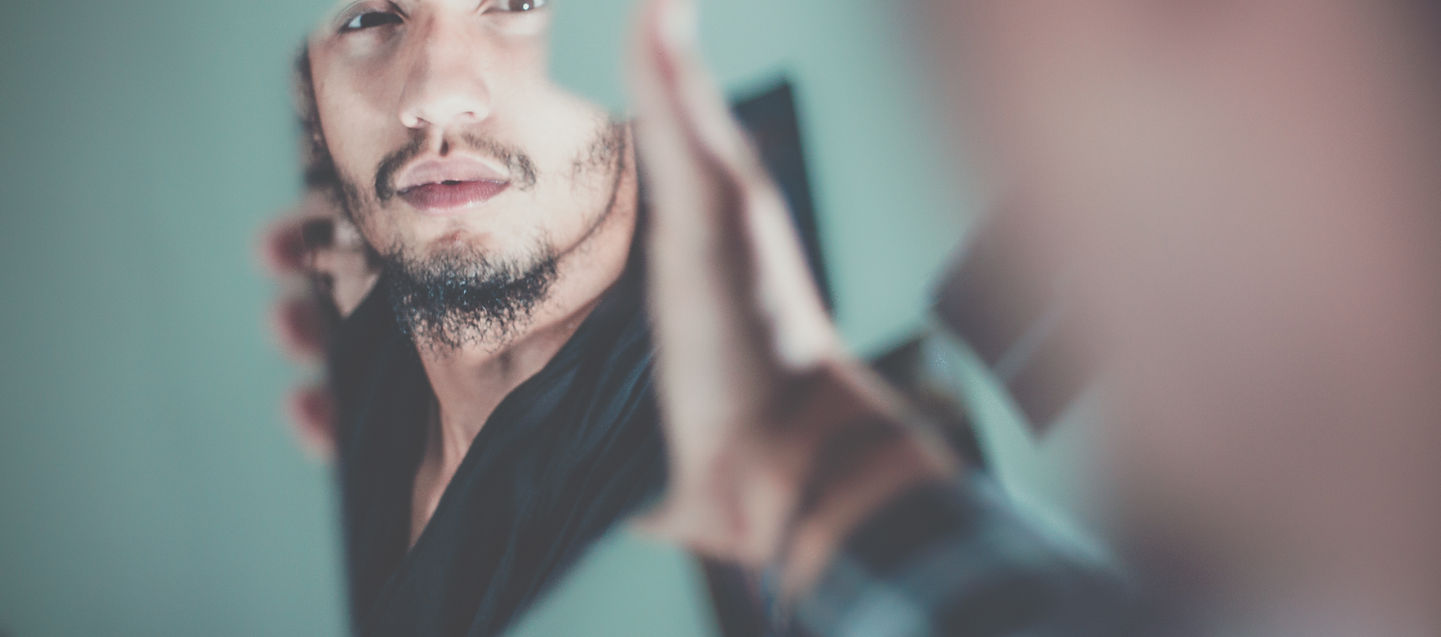 Man smiling confidently in mirror – symbolising reprogramming self-belief and speaking truth into being.