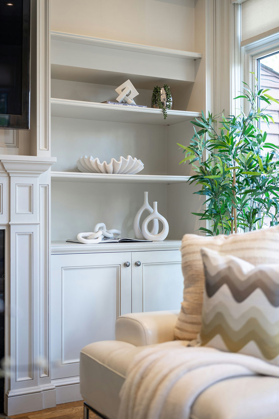 White shelves with abstract decor, books, and a potted plant. Cozy atmosphere with a cream sofa, zigzag pillow, and a soft blanket.