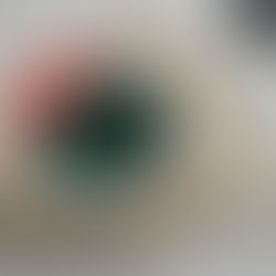 Punch needle craft embroidery hoop with pink, green, and dark green abstract floral design on beige fabric, with a gray yarn ball in the background on a white surface.