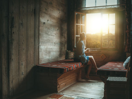 A woman sitting by a sunlit window in the early morning, soft warm light falling across her face — representing circadian rhythm and morning light exposure in perimenopause - from Vibrance Way 