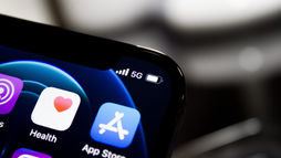 Close-up of a smartphone screen showing app icons, 5G signal, and battery indicator. Background is blurred, with a dark and techy mood.