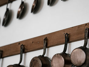 Copper pots and pans hang from wooden racks on a white wall, creating a rustic and organized kitchen setting.