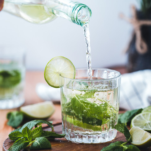 Mojito cocktail being poured into a tumbler glass with fresh mint leaves and lime slices