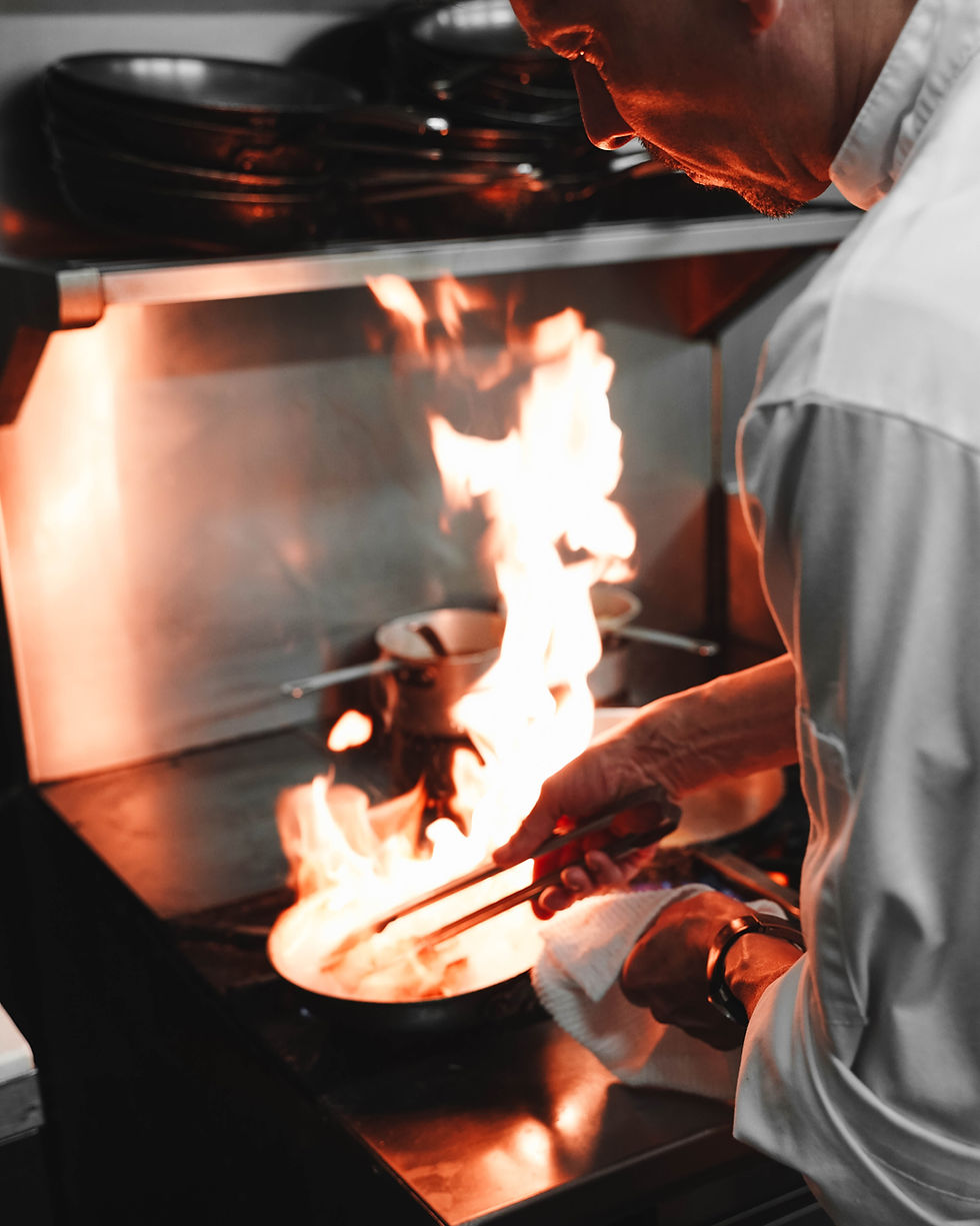 Chef flambéing dish in professional kitchen with high flame