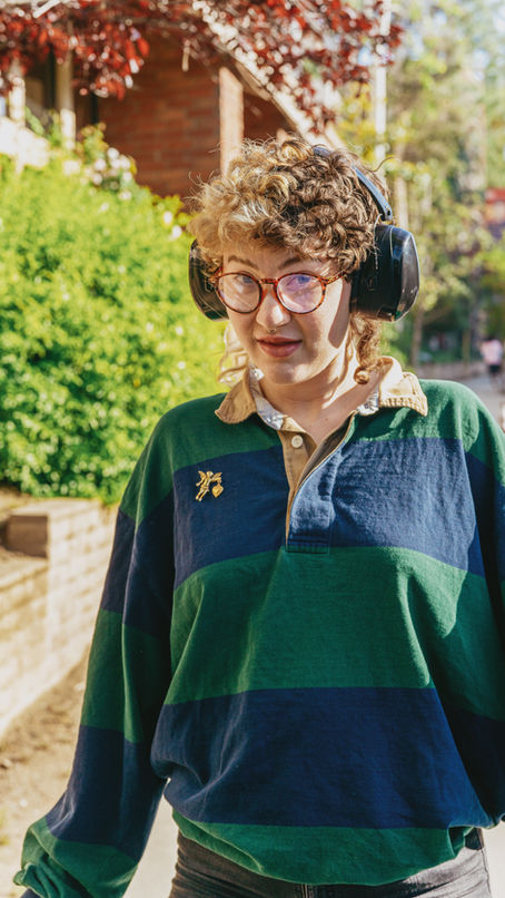 Person wearing noise cancelling headphones and glasses with curly hair looking at the camera.