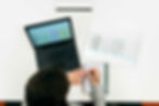 Person notiert Notizen neben Laptop und Plan