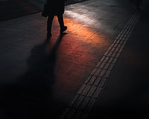 Silhouetted person walking on a tiled station platform, long shadow cast in warm orange light.