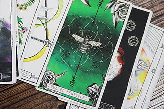 A close up photo of a Tarot card, the Four of Pentacles. It is primarily green and shows a drawn bee in the center of intersecting circles and four pentacles around it.