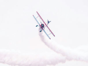 a red and blue airplane leans hard on its left wing with a trail of smoke behind it
