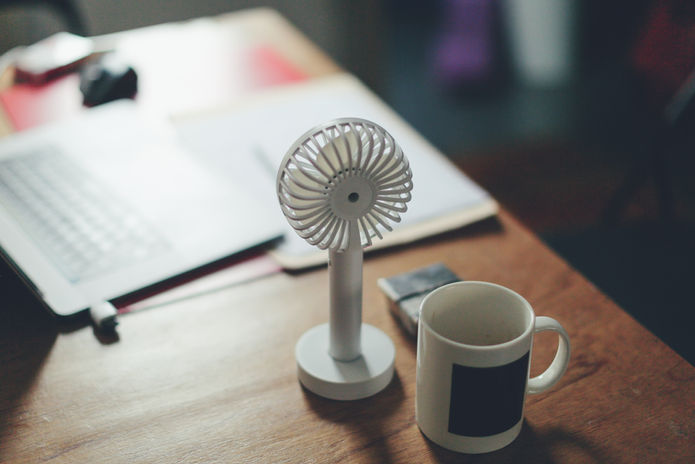 Small portable desk fan beside a mug on a work surface.