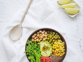 Vibrant salad bowl with avocado, chickpeas, peas, corn, lettuce, flaxseeds, and red paste on a white background. Sliced lemon nearby.