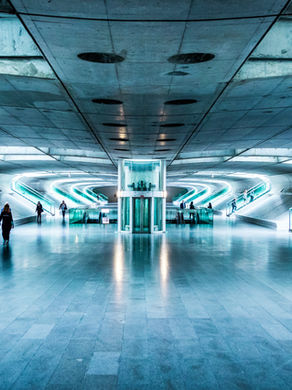 Futuristic blue-lit tunnel with people walking, escalators on both sides, and a central glass elevator. Mood is modern and sleek.