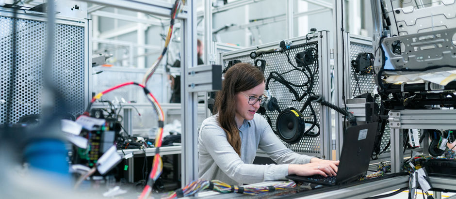 Woman working on a laptop in a robotics engineering lab, representing business valuation in technical or asset-heavy industries.