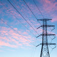 High-voltage transmission tower and power lines silhouetted against a pastel pink-and-blue cloudy sky at sunset