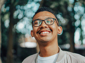 Smiling man with glasses in a sunlit park, close-up portrait with blurred trees in the background