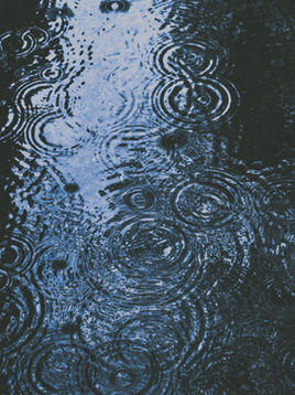 Rain drops fall in a large, dark puddle of water on the street.