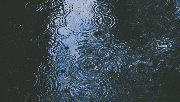 Rain drops fall in a large, dark puddle of water on the street.
