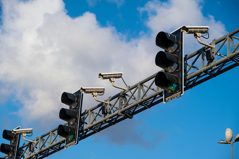 Traffic cameras and lights on a metal pole against a blue sky with clouds. Green light visible, with a calm, clear atmosphere.