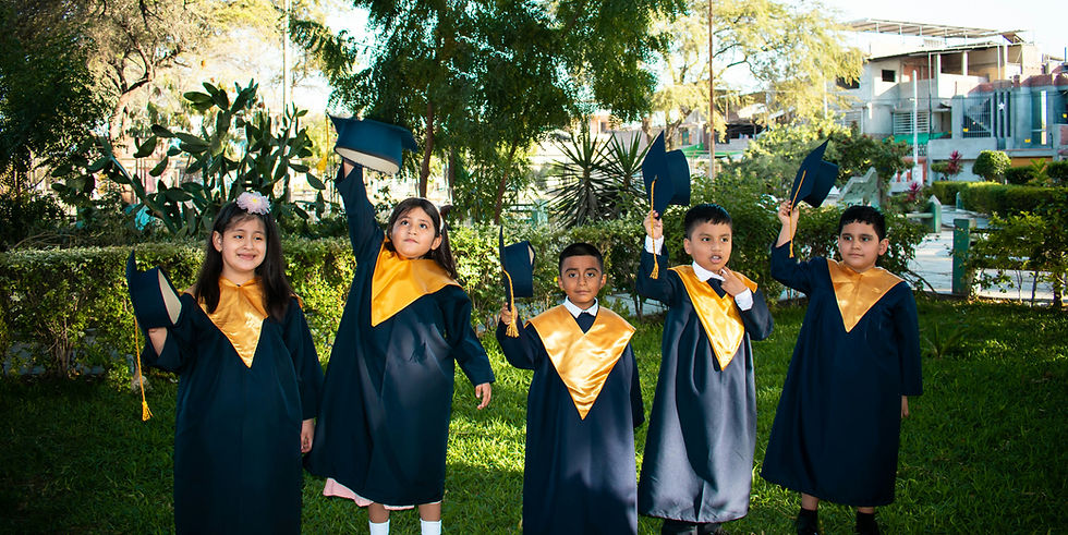 Five children in navy-and-gold graduation gowns smile and hold caps in a sunny garden with trees and houses behind them