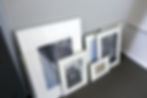 Framed black-and-white photos leaning against a wall in a gray-carpeted room. One frame shows "550Ti" text. Minimalist, organized setting.