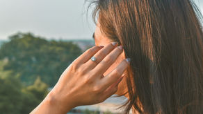A woman in her 40s touching her ear with a thoughtful expression in soft morning light, representing perimenopause tinnitus and unexplained ringing in the ears during hormonal transition from Vibrance Way