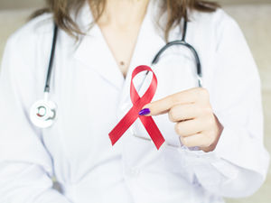 A doctor wearing a her coat and a stethoscope holding a red ribbon symbolizing HIV.