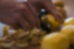 Hands peeling potatoes with a black peeler, surrounded by potato skins on a wooden surface. Warm lighting creates a cozy kitchen feel.