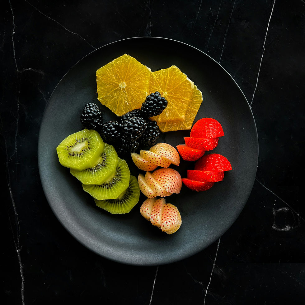 Colorful sliced fruit arranged on a black plate: orange, blackberry, kiwi, and strawberry on a dark marble background.