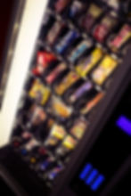 Vending machine filled with colorful snacks like Twix and Snickers. Brightly lit with blue-lit keypad on the side.