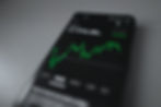 Smartphone displaying a Bitcoin price chart at €47,596.00. Green line graph indicates upward trend. Black background, minimal interface.