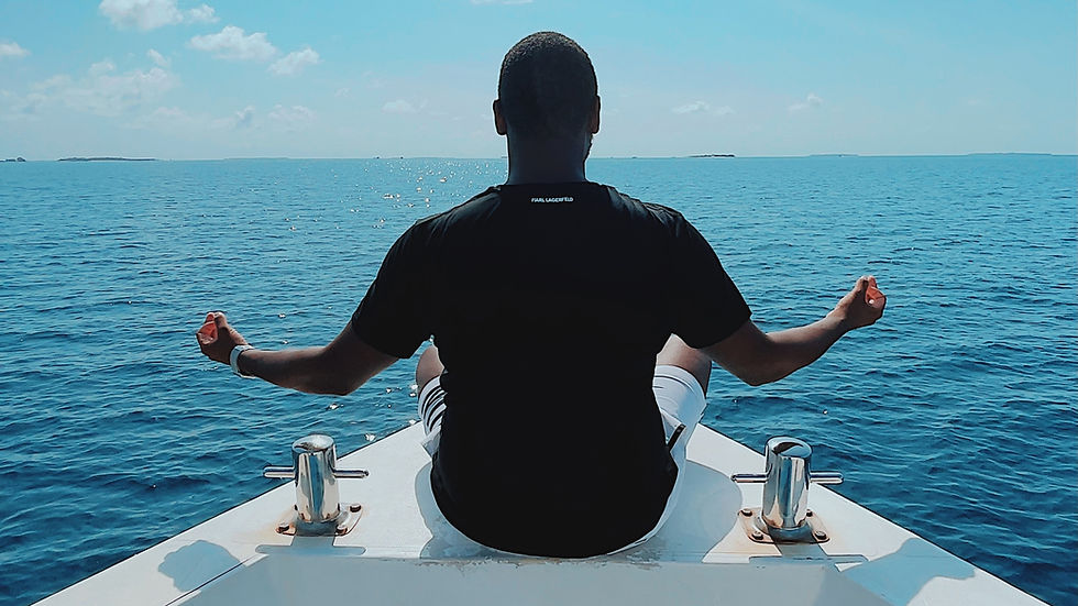A person meditates at the front of a boat on calm blue ocean. They wear a black shirt, and the sky is bright and clear, creating a serene mood.