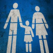 White family restroom symbol on a worn blue floor, showing a man, woman, and child holding hands.