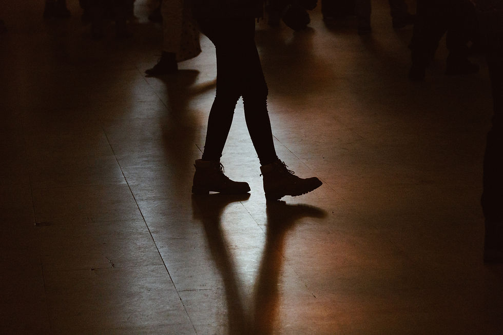 Silhouetted legs in boots walking on a polished floor, casting shadows in a dimly lit space, conveying a sense of movement and mystery.